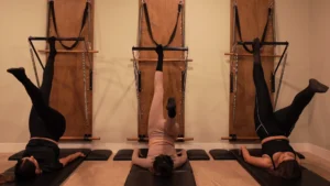 TRES CHICAS REALIZANDO UNA POSTURA DE PILATES EN MÁQUINA SPRINGBOARD
