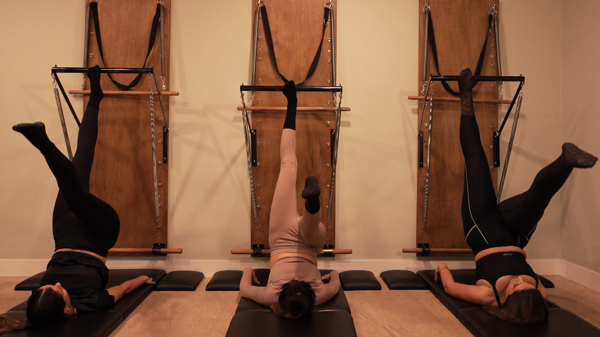 TRES CHICAS REALIZANDO UNA POSTURA DE PILATES EN MÁQUINA SPRINGBOARD